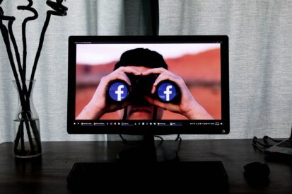 man holding binoculars on desktop with facebook logo in lenses