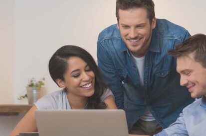 a group of 3 people looking at a computer together at the table