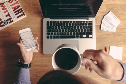 A desk with office supplies and computer and someone holding black coffee