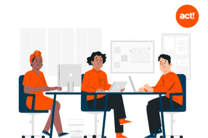 Three people sitting at a table working on their computers wearing orange with an Act! logo in the top right corner.